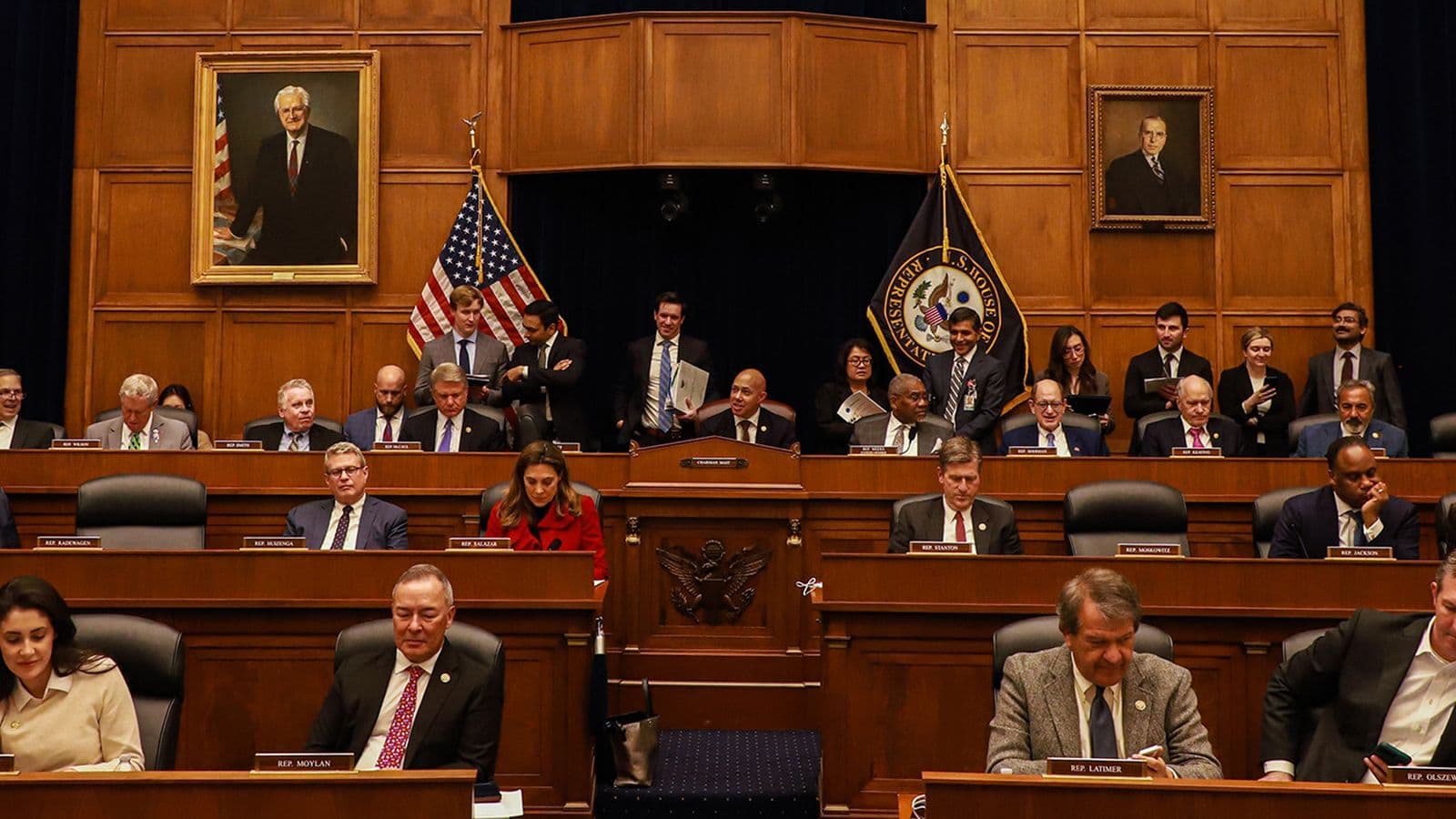 House Foreign Affairs Committee members seated at the dais of the committee's hearing room, with the US flag and committee seal flanking the chairman's center position.