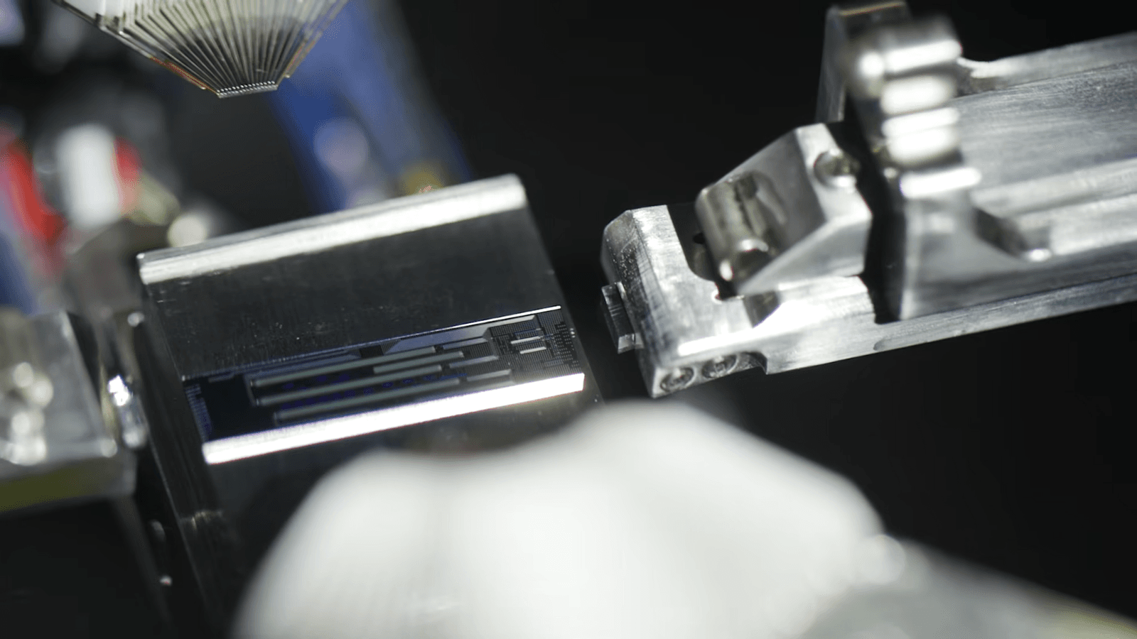 Close-up of a fiber-optic array being aligned with a photonic chip held in a precision metal fixture during lab assembly of Cisco's Universal Quantum Switch prototype.